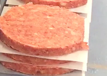 Hamburguesas apiladas con papel intermedio en la cinta transportadora de una máquina RM Sertec